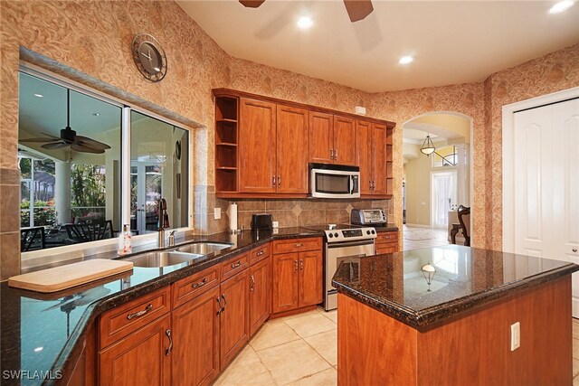 kitchen featuring stainless steel appliances, sink, dark stone countertops, a kitchen island, and light tile patterned flooring