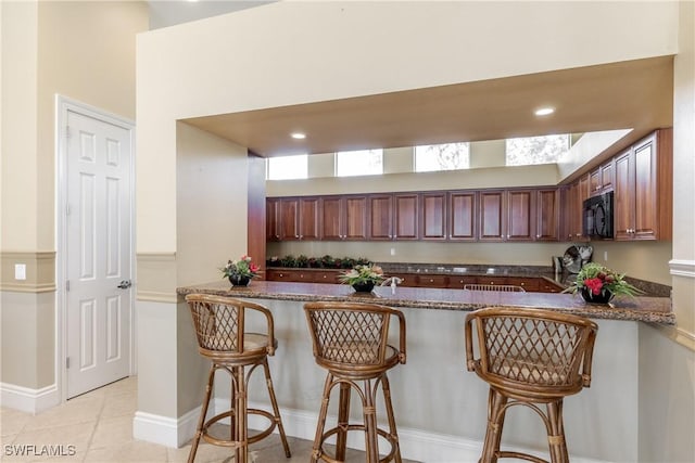 kitchen featuring kitchen peninsula, a kitchen breakfast bar, light tile patterned flooring, and dark stone countertops