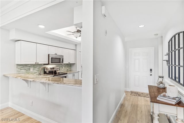 kitchen with kitchen peninsula, appliances with stainless steel finishes, decorative backsplash, light hardwood / wood-style flooring, and white cabinets