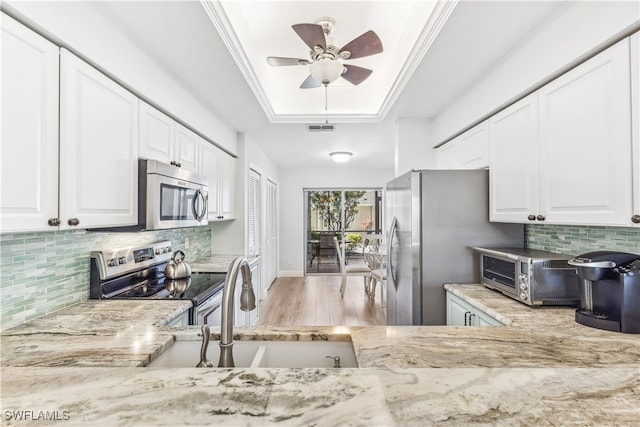 kitchen featuring ceiling fan, stainless steel appliances, light hardwood / wood-style flooring, decorative backsplash, and white cabinets