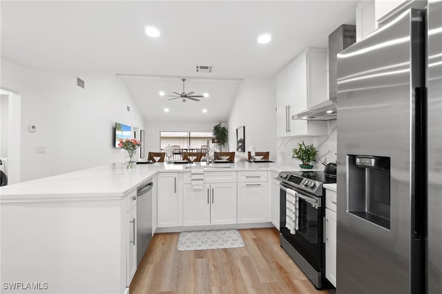 kitchen featuring wall chimney exhaust hood, stainless steel appliances, backsplash, kitchen peninsula, and lofted ceiling