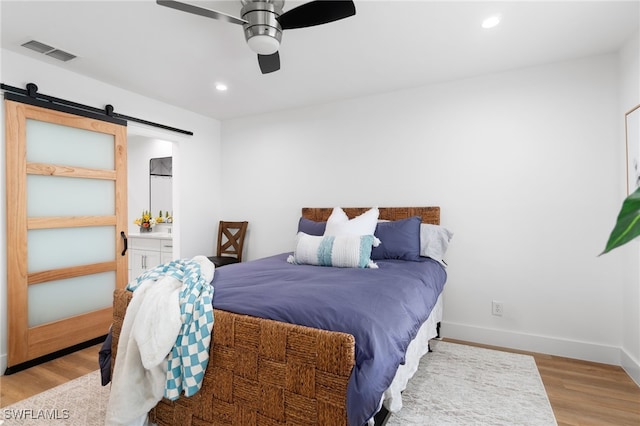 bedroom featuring ceiling fan, a barn door, light wood-type flooring, and ensuite bathroom