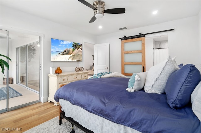 bedroom featuring a barn door, access to outside, light hardwood / wood-style flooring, and ceiling fan