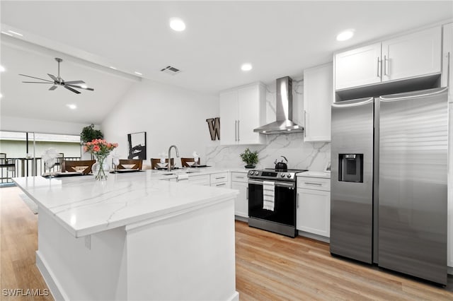 kitchen featuring lofted ceiling with beams, white cabinets, stainless steel appliances, and wall chimney range hood