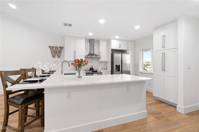 kitchen with kitchen peninsula, appliances with stainless steel finishes, white cabinets, and wall chimney exhaust hood