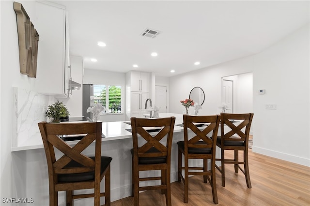 kitchen with white cabinets, a kitchen bar, light hardwood / wood-style flooring, and sink