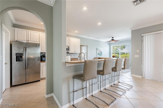 kitchen with white cabinets, a kitchen bar, stainless steel appliances, and light tile patterned flooring