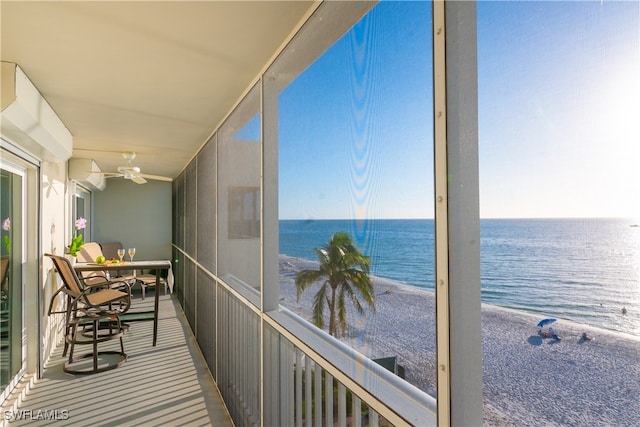 sunroom with ceiling fan, a water view, and a view of the beach