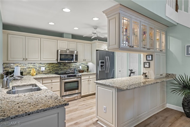 kitchen featuring appliances with stainless steel finishes, a sink, a peninsula, and light wood finished floors