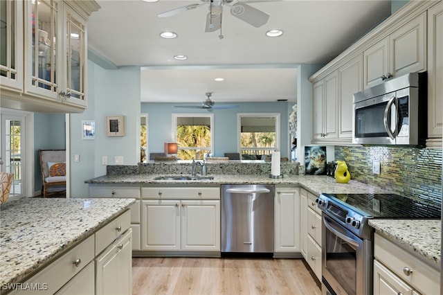 kitchen with tasteful backsplash, light stone counters, stainless steel appliances, light wood-style floors, and a sink