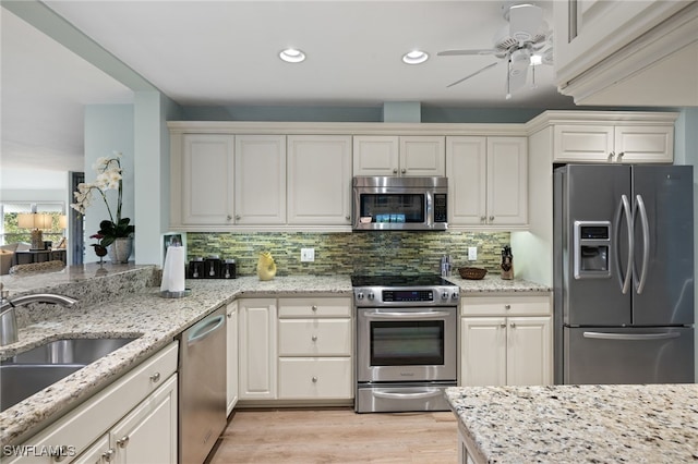 kitchen with light wood finished floors, appliances with stainless steel finishes, a sink, and tasteful backsplash