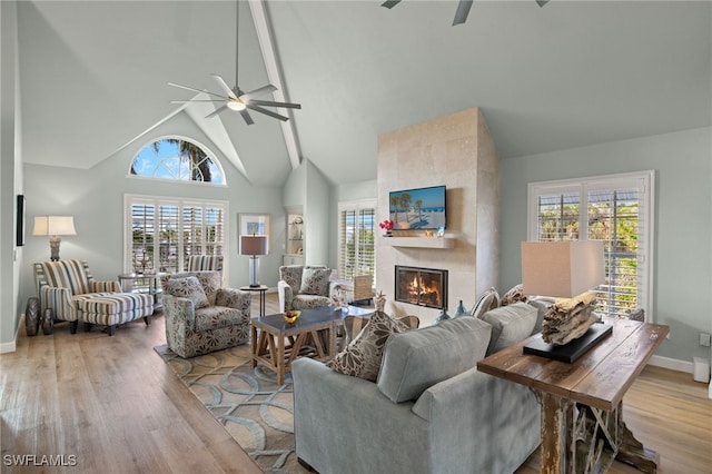 living area with high vaulted ceiling, plenty of natural light, a tile fireplace, and light wood-style flooring