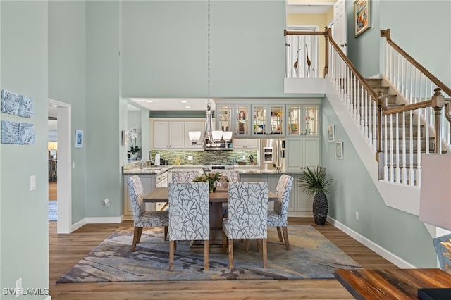 dining space featuring dark wood-type flooring, a towering ceiling, stairway, and baseboards