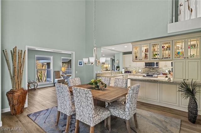 dining space with baseboards, a notable chandelier, a high ceiling, and wood finished floors