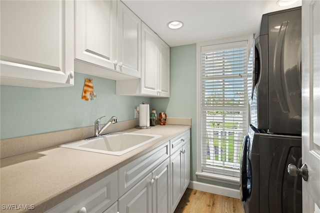 clothes washing area featuring cabinet space, baseboards, stacked washer and clothes dryer, light wood-style flooring, and a sink