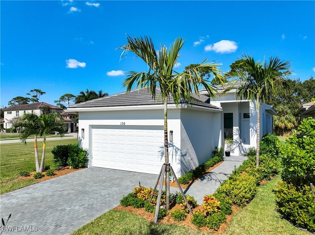 single story home featuring stucco siding, decorative driveway, a front yard, an attached garage, and a tiled roof