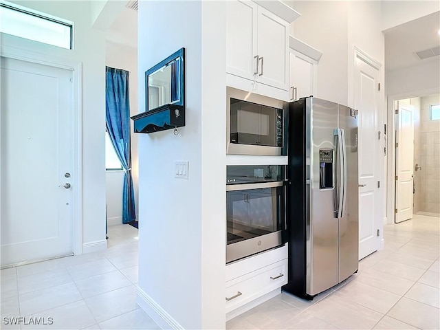 kitchen with appliances with stainless steel finishes, light tile patterned floors, white cabinetry, and plenty of natural light