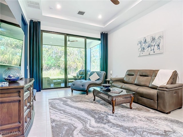 tiled living room with ceiling fan and a raised ceiling