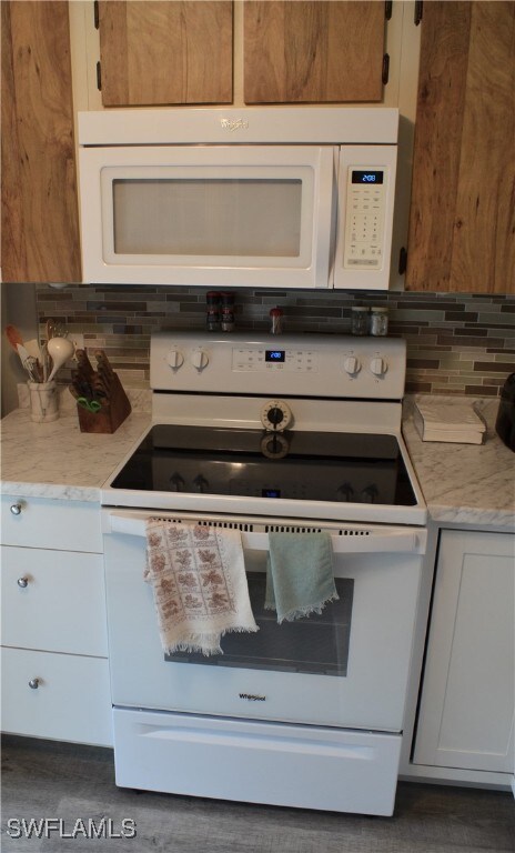 kitchen with white cabinetry, light stone counters, white appliances, and backsplash