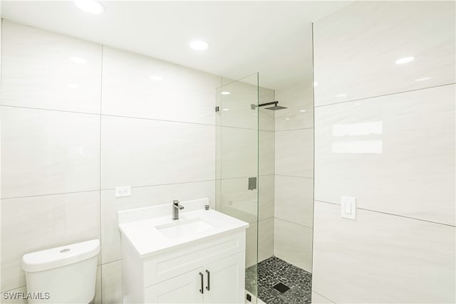 bathroom with a tile shower, vanity, tile walls, and toilet