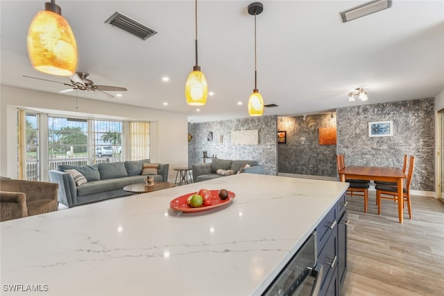 kitchen featuring ceiling fan, light hardwood / wood-style floors, light stone countertops, and hanging light fixtures