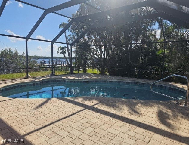 view of pool with a patio area, a water view, and glass enclosure