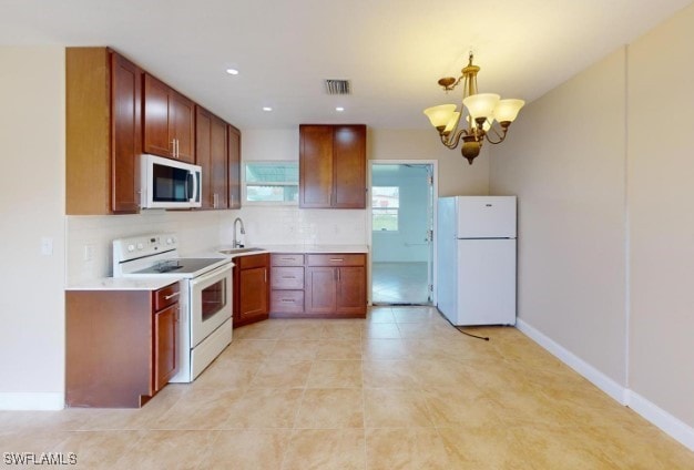 kitchen featuring backsplash, white appliances, sink, pendant lighting, and an inviting chandelier