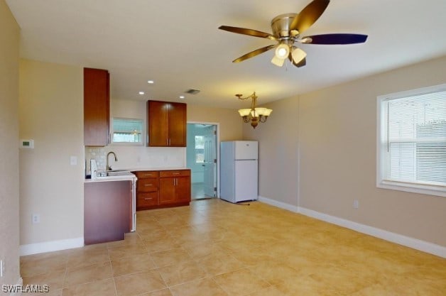 kitchen featuring backsplash, ceiling fan with notable chandelier, sink, decorative light fixtures, and white fridge