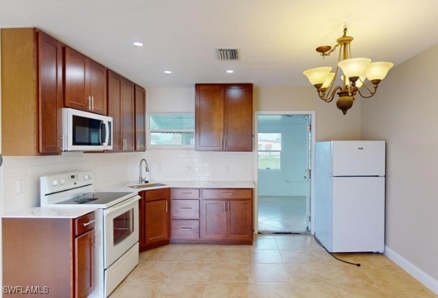 kitchen featuring decorative backsplash, white appliances, sink, pendant lighting, and a chandelier