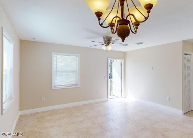 tiled spare room with ceiling fan with notable chandelier and a healthy amount of sunlight