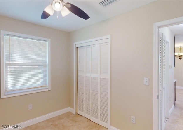 unfurnished bedroom featuring a closet, light tile patterned floors, and ceiling fan with notable chandelier