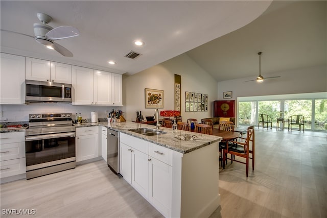 kitchen with kitchen peninsula, stainless steel appliances, sink, white cabinetry, and lofted ceiling