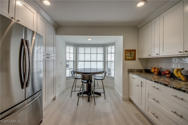 kitchen featuring dark stone counters, white cabinets, tasteful backsplash, light hardwood / wood-style floors, and stainless steel refrigerator