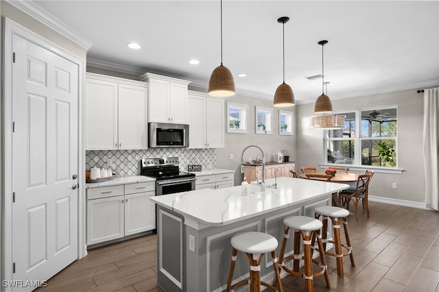 kitchen featuring appliances with stainless steel finishes, decorative light fixtures, white cabinetry, an island with sink, and a breakfast bar