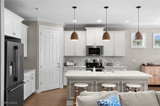 kitchen with stainless steel appliances, white cabinetry, a center island with sink, and decorative light fixtures