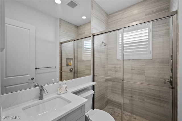 bathroom featuring toilet, a stall shower, vanity, and visible vents