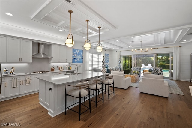 kitchen with decorative light fixtures, a center island with sink, dark hardwood / wood-style floors, and wall chimney range hood