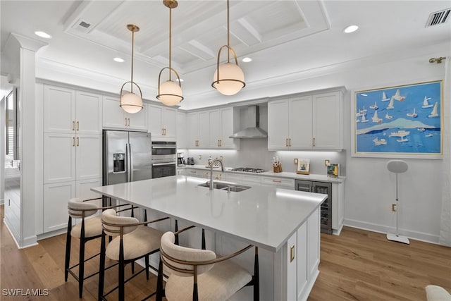 kitchen with sink, stainless steel appliances, wall chimney range hood, light hardwood / wood-style flooring, and decorative light fixtures