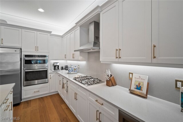 kitchen with white cabinets, wall chimney exhaust hood, light wood-type flooring, and appliances with stainless steel finishes