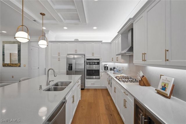 kitchen featuring sink, hanging light fixtures, wall chimney range hood, appliances with stainless steel finishes, and light wood-type flooring