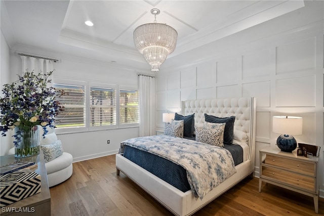 bedroom with a raised ceiling, wood-type flooring, and an inviting chandelier