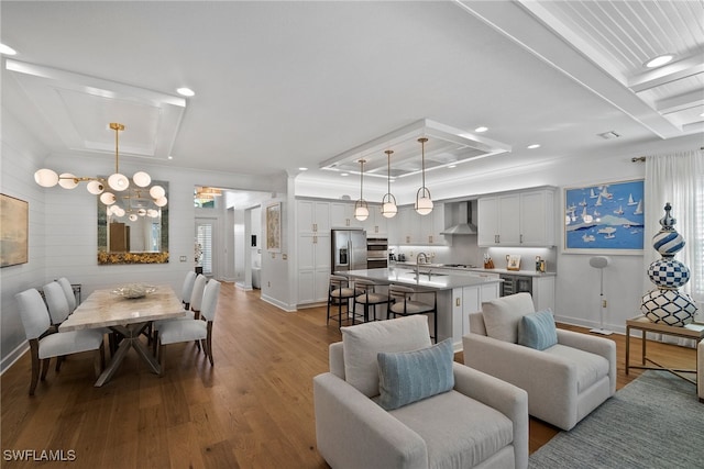 living room featuring crown molding, light wood-type flooring, a tray ceiling, a notable chandelier, and beverage cooler