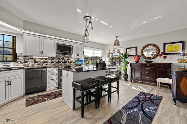 kitchen with light wood-type flooring, tasteful backsplash, stainless steel appliances, decorative light fixtures, and a breakfast bar area