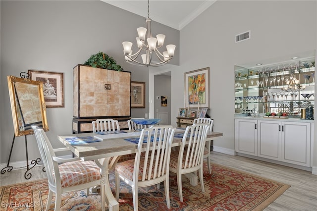 dining room with crown molding, light hardwood / wood-style flooring, a towering ceiling, and an inviting chandelier