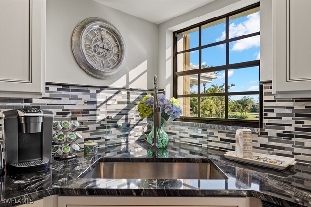 kitchen featuring decorative backsplash, sink, white cabinetry, and dark stone countertops