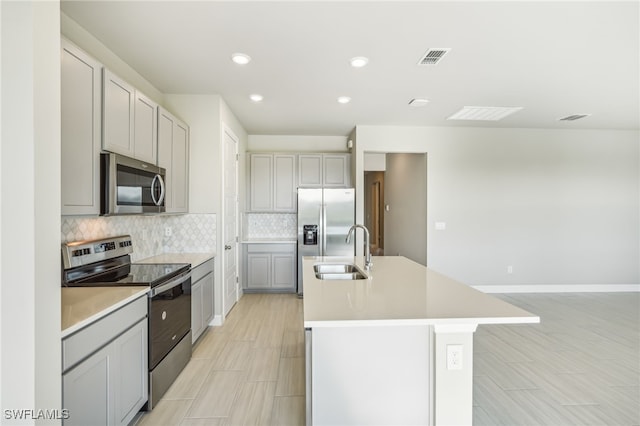 kitchen featuring appliances with stainless steel finishes, backsplash, a kitchen island with sink, sink, and gray cabinets