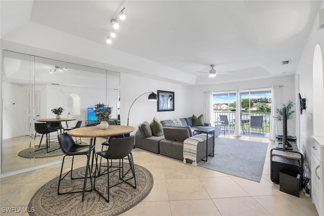 tiled living room with ceiling fan and a raised ceiling