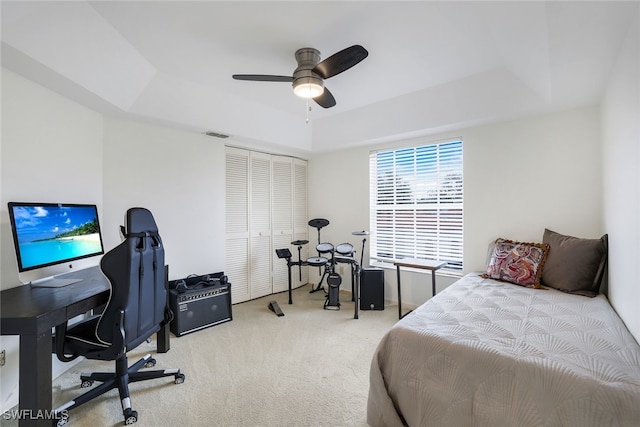 carpeted bedroom featuring ceiling fan, a raised ceiling, and a closet