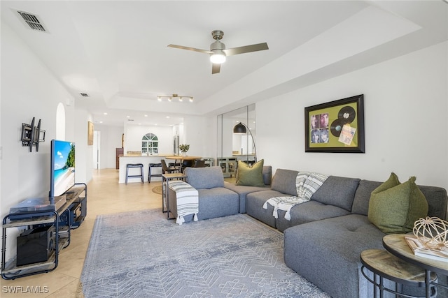 tiled living room featuring ceiling fan and a tray ceiling