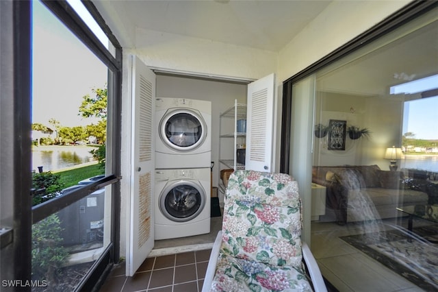 clothes washing area with dark tile patterned floors, a water view, and stacked washer / dryer